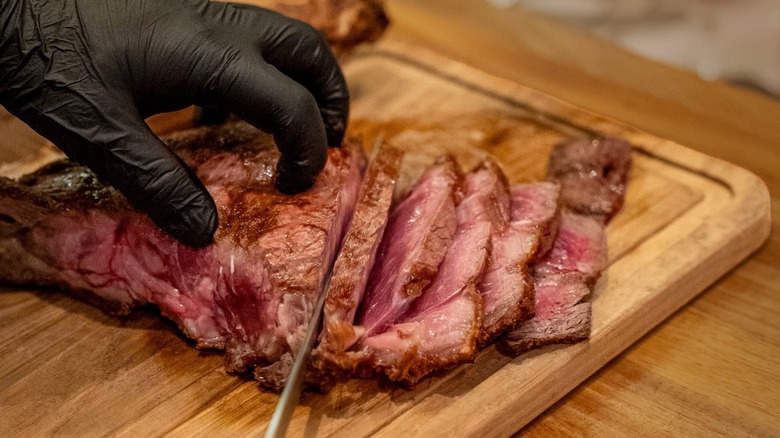 Hands slicing steak on a wooden board
