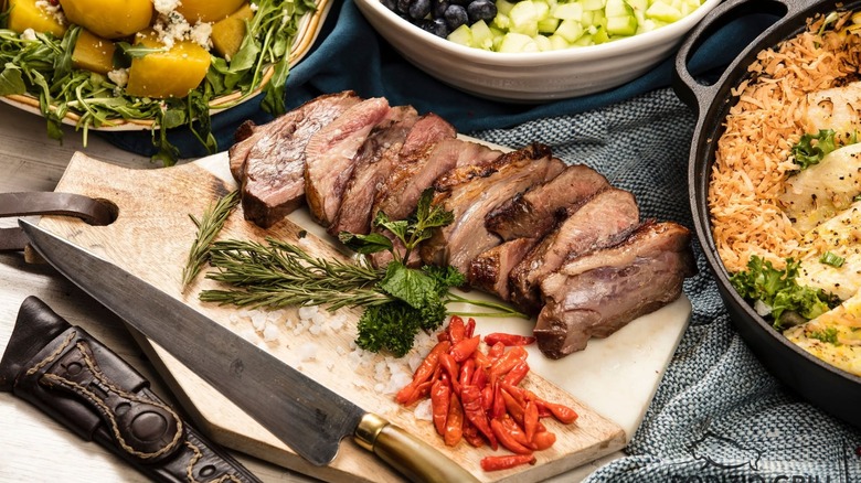 Sliced steak on a wooden board with rosemary and other dishes