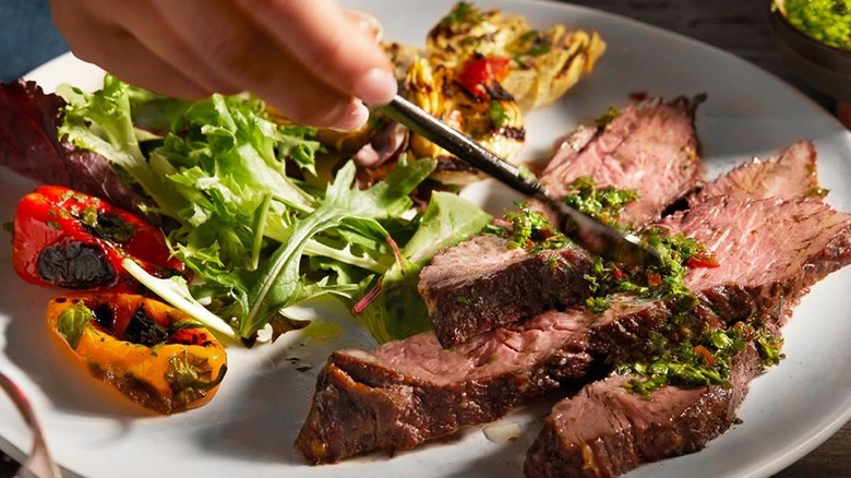 Slices of steak on a plate with greens and roasted veg