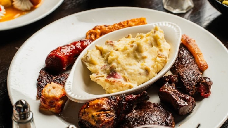 Assortment of meats on a plate with a bowl of mashed potatoes