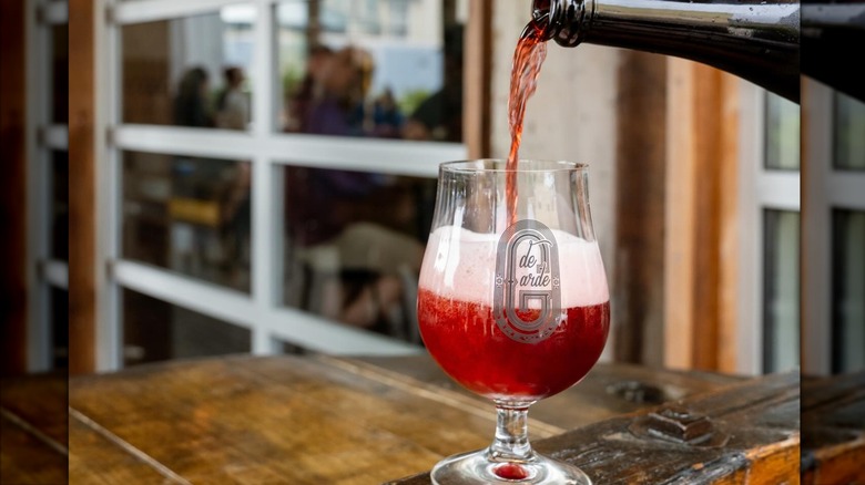 Pouring red beer into a glass on wooden table outside