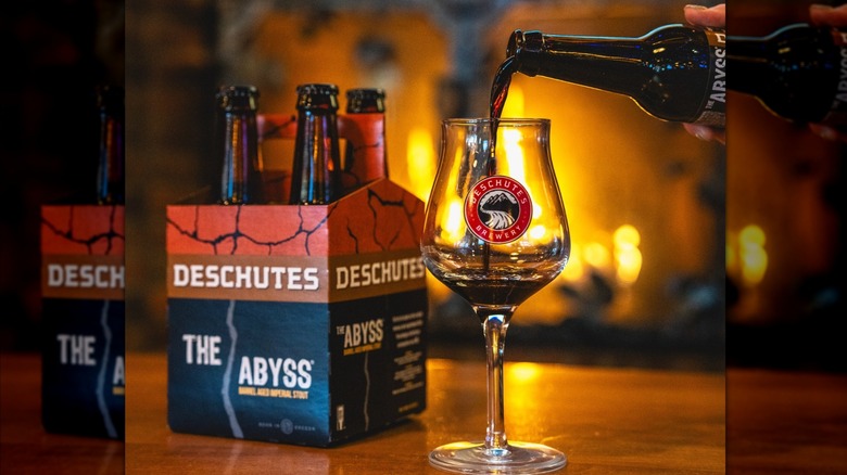 Beer being poured into a glass alongside a four-pack of bottles with fireplace blurred in background