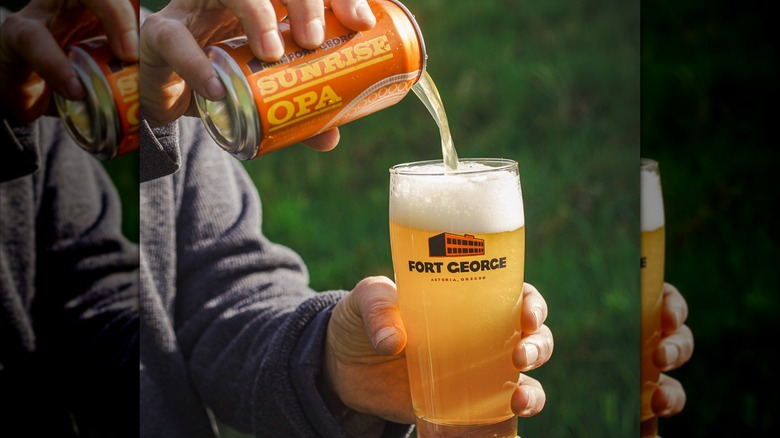 Hands pouring a can of Sunrise OPA beer into a pint glass outside