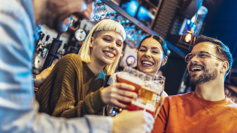 Group of four friends smiling and toasting with pint glasses of beer