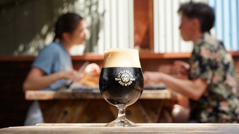 Glass of dark beer on table with people blurred in background