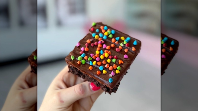 Hand holding brownie topped with frosting and sprinkles