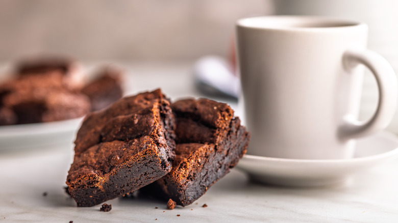 Two chocolate brownies on plate next to coffee cup