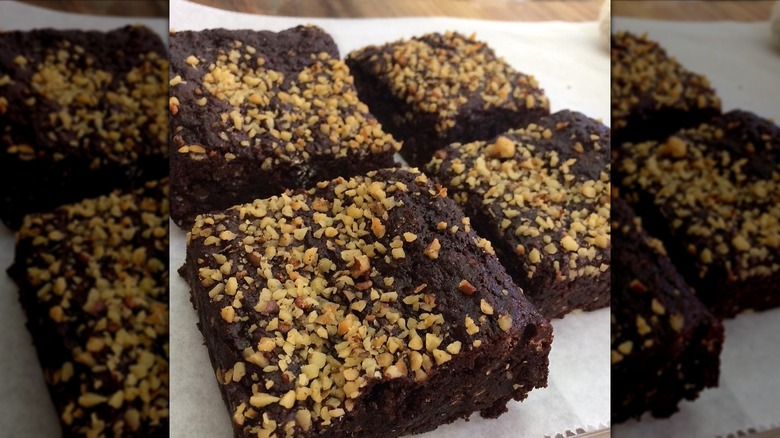 Four brownies topped with chopped walnuts on parchment paper