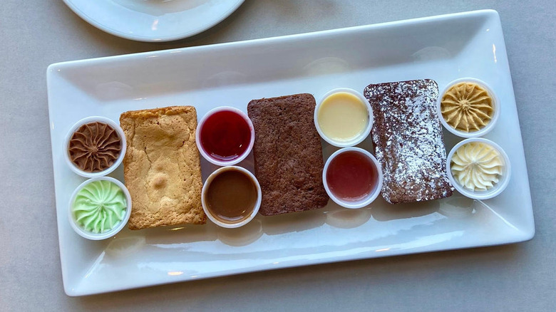 Three types of brownies surrounded by various sauces and frosting on rectangular plate