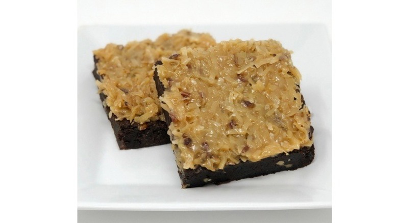 Two German chocolate brownies topped with coconut on plate