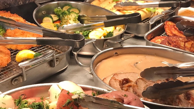 Buffet of meat and vegetables in metal pans on a metal table