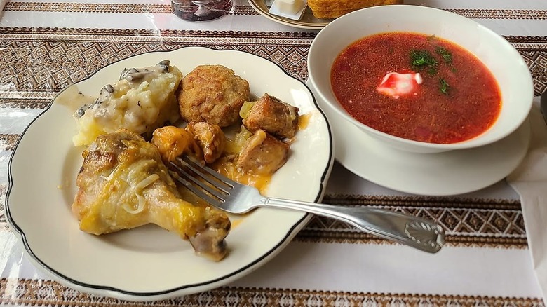 Plate of chicken and potatoes and a bowl of borscht on a decorative tablecloth