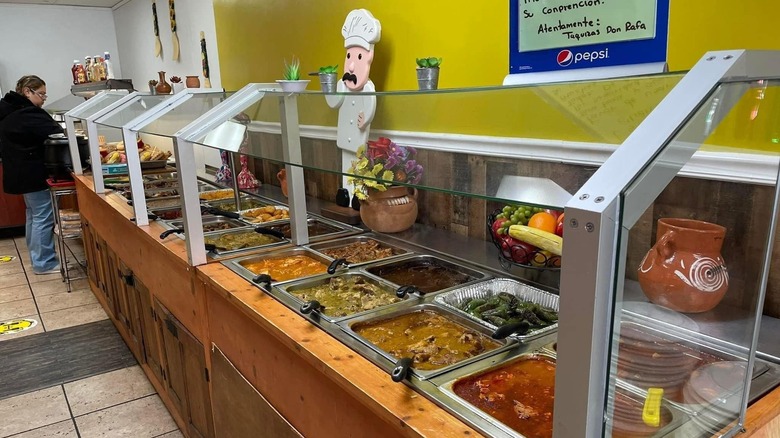Wooden buffet of Mexican food with one diner and a yellow wall