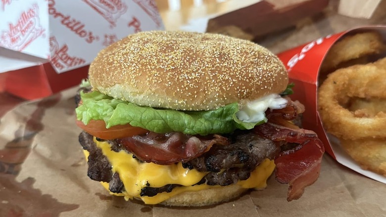 A Portillo's Double Bacon Cheeseburger sitting next to a container of onion rings