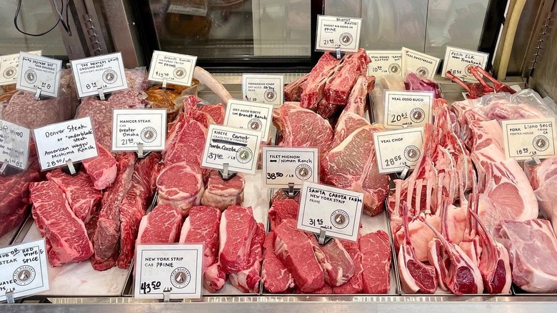 Butcher shop display case with fresh cuts of meat and price tags.