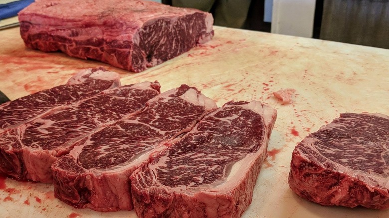 Butcher block with well-marbled steaks and roast in background.