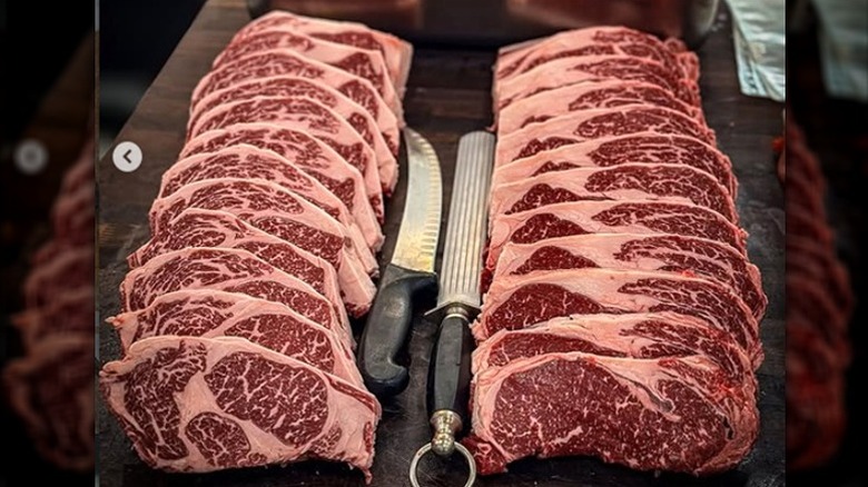 Butcher block with two rows of sliced fresh raw ribeye and NY strip.