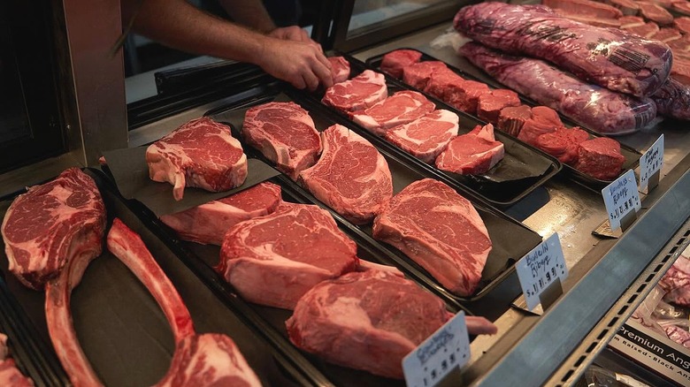 Hand placing meat in a butcher display case with other fresh cuts of meat.