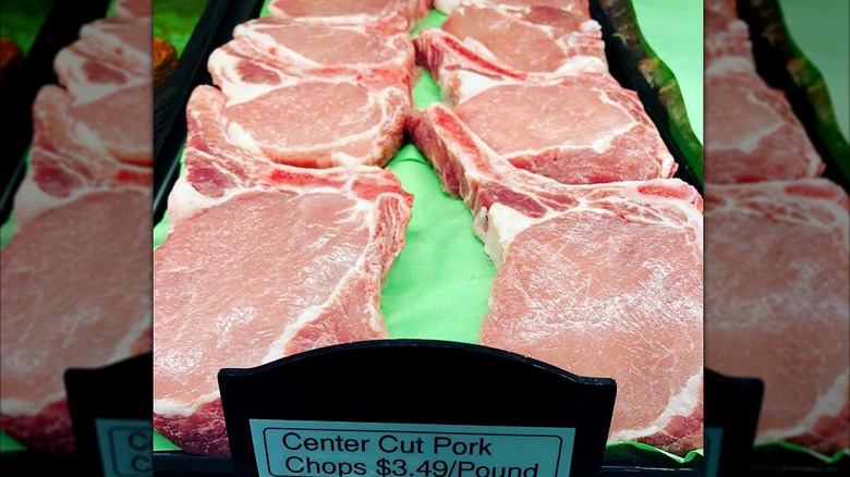Two rows of fresh cuts of pork chops with price tag.