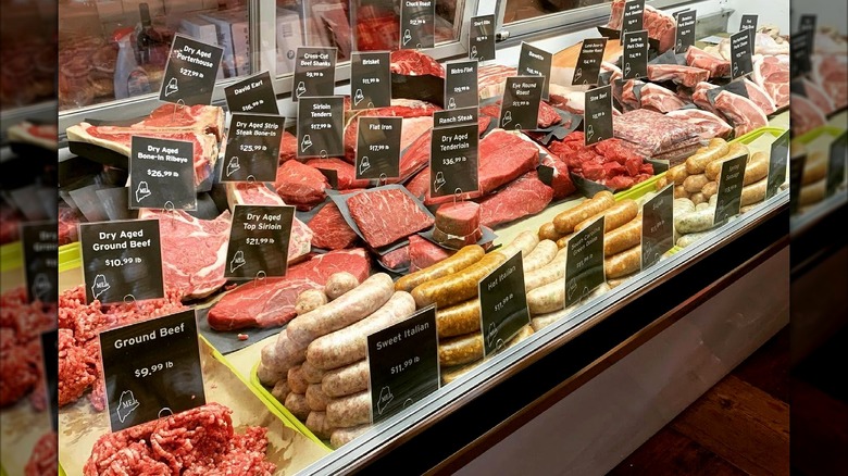 Butcher shop display case with fresh cuts of meat and price signs.