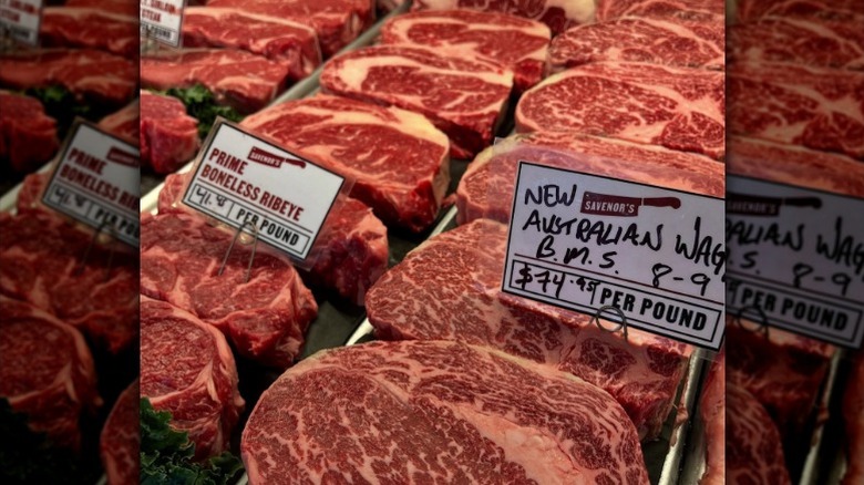 Raw cuts of meat displayed in butcher case with price signs.