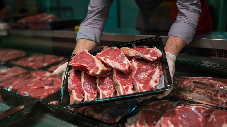 Hands holding a tray of raw fresh cut beef steaks.