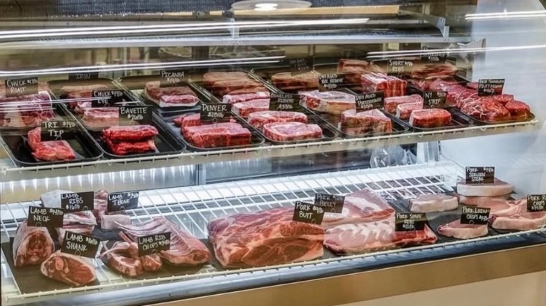 Raw cuts of meat in a butcher shop display case.