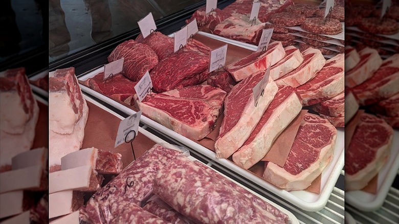Raw cuts of meat in butcher display case.