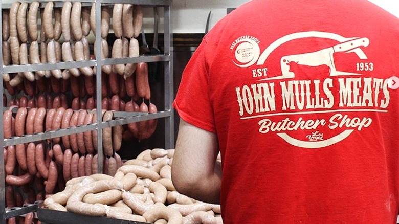 Person with John Mull's Meat shirt standing in front of racks of sausages.