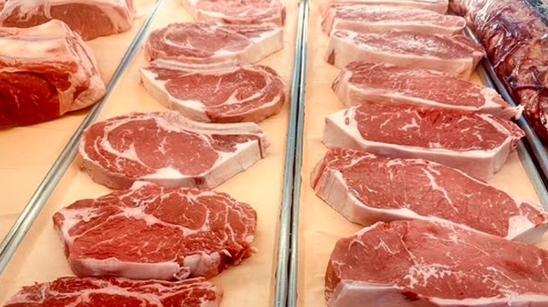Fresh cut ribeye and New York strip in butcher display case.