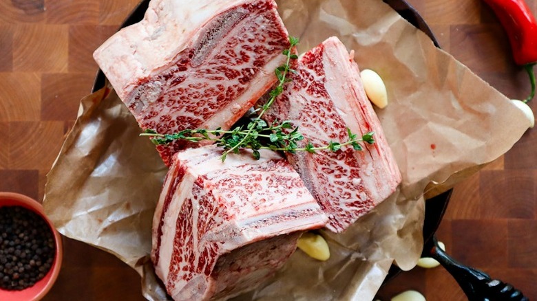 Chunks of fresh raw meat on butcher paper with sprigs of herbs on top.