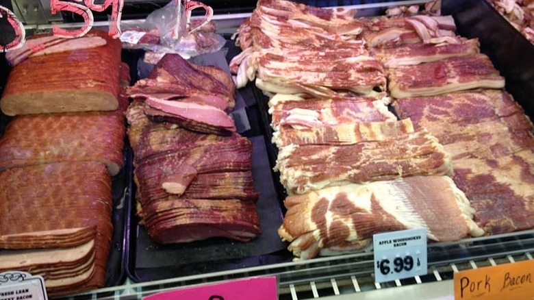 Rows of smoked meats like ham and bacon in butcher display case.