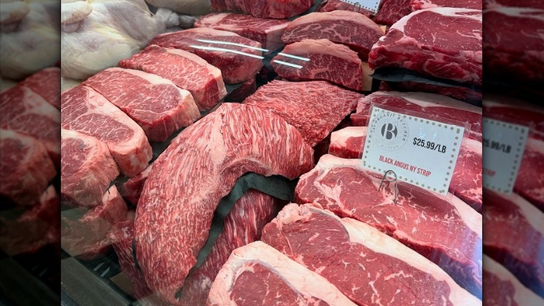Fresh raw cuts of beef in butcher display case.
