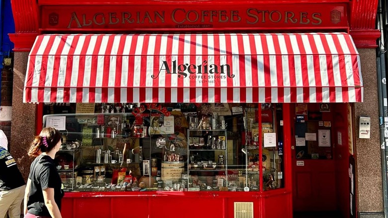 Woman walking past the exterior ofAlgerian Coffee Stores with a red striped awning