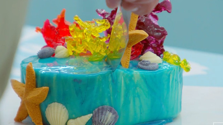 An ocean themed cake with sea stars, shells, and coral on a white table.