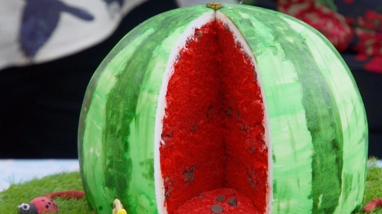 A watermelon shaped cake on top of makeshift grass with lady bugs.