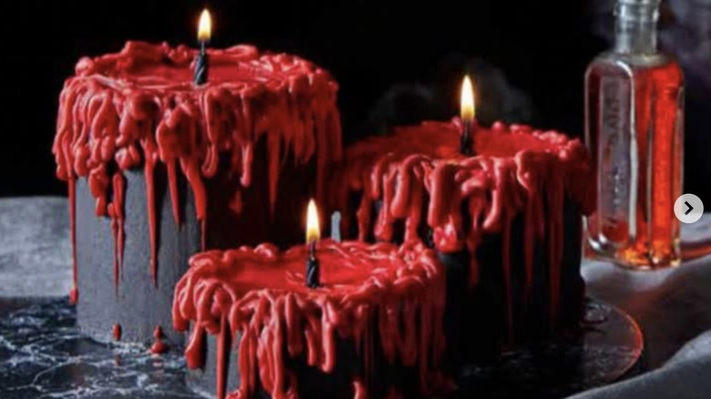 Black cakes that look like candles with red frosting "wax" on a black table with a bottle of whiskey.
