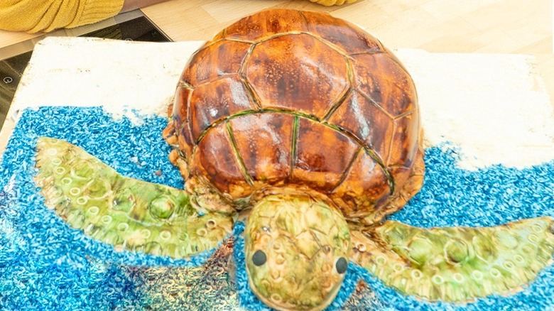 A lifelike turtle shaped cake on top of blue ocean icing on a table.