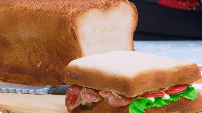 A cake made to look like a sandwich on a wood cutting board on a table.