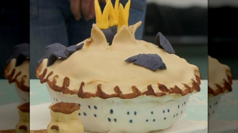 A cake made to look like a pie with blackbirds sticking out of it and decorated with black feathers.