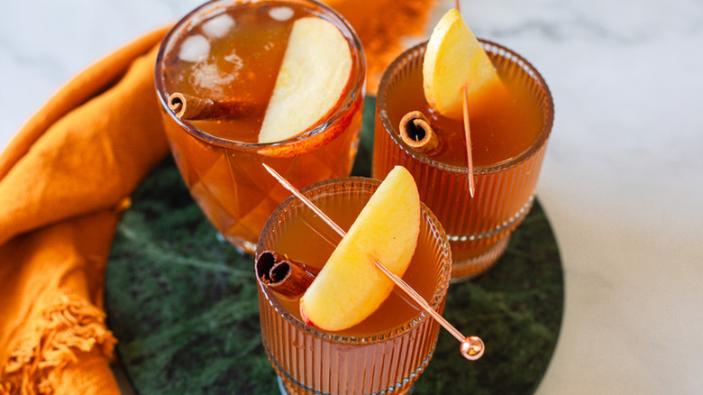 Three cinnamon apple chai kombucha drinks in glasses, garnished with skewered apple wedges