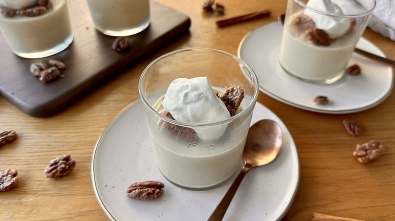Vanilla chai pudding in dessert glasses, each topped with whipped cream and pecans