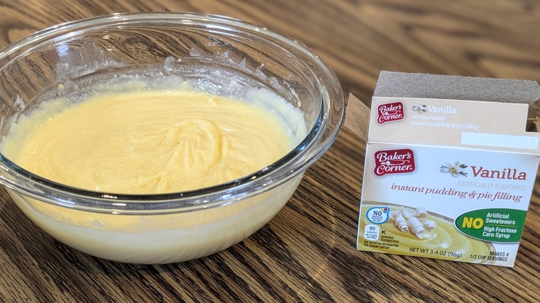 Large mixing bowl of pudding next to open box of pudding mix on wooden table