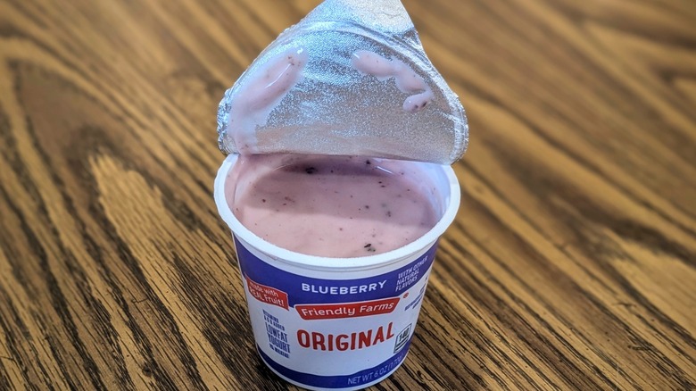 Individual cup of blueberry yogurt with lid peeled back sitting on a wooden table