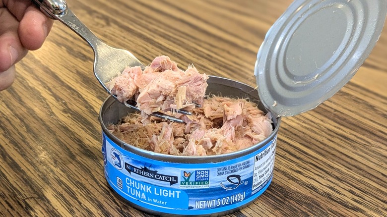 Hand pulling tuna chunks out of a can with a fork