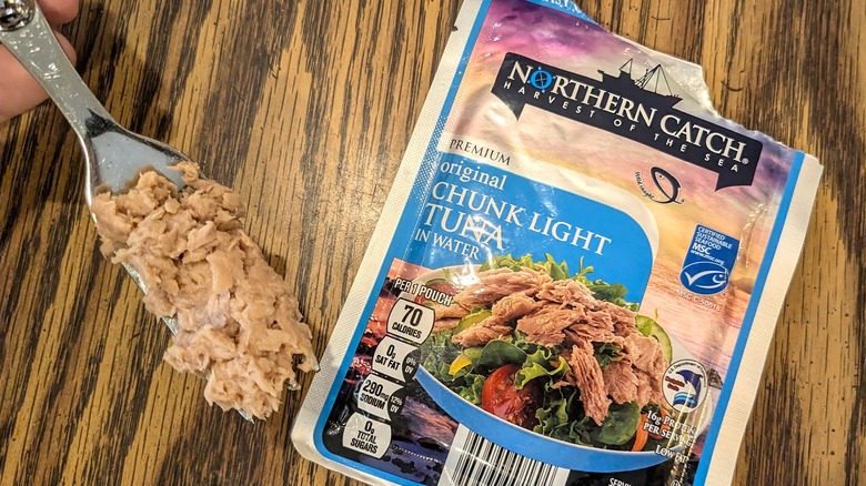 Tuna on a fork next to open tuna pouch on wooden table