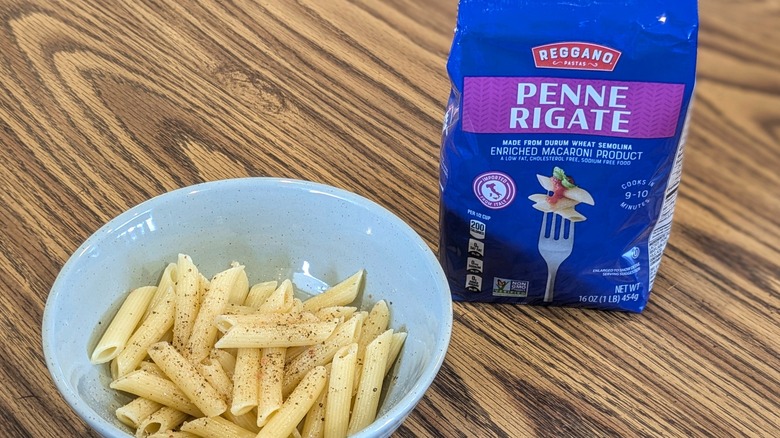 Bowl of cooked pasta next to a pasta bag on wooden table