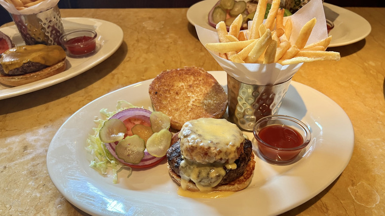 Macaroni and cheese burger sits on a  plate with a tin cup of fries and some ketchup