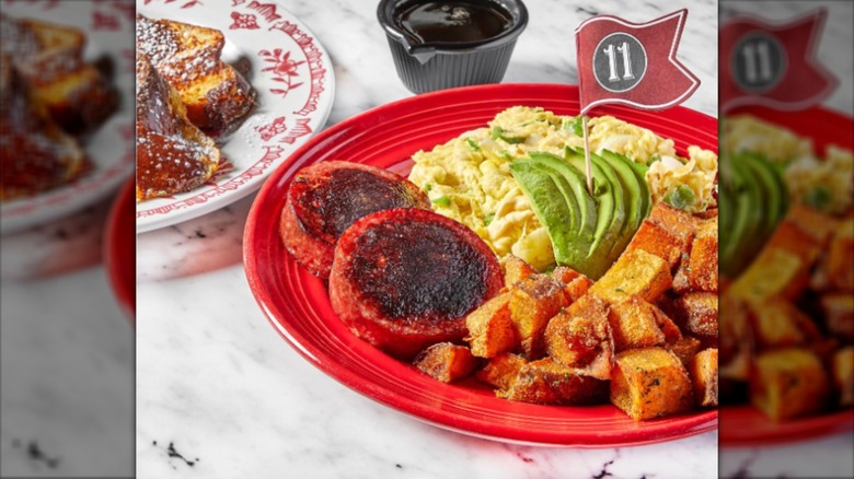 Breakfast plate with eggs, avocado, and potatoes, with French toast in background