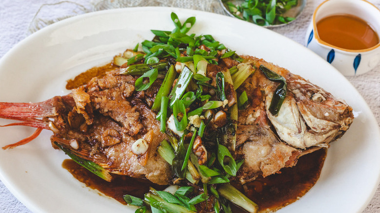 Whole pan-fried tilapia on serving plate, garnished with chopped scallions